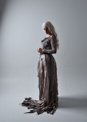 full length portrait of girl wearing old torn wedding dress. standing pose with rim lighting on a grey studio background.