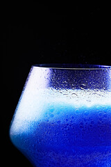 Blue drink is poured into a glass. Black background.