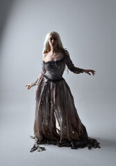 full length portrait of girl wearing old torn wedding dress. standing pose with rim lighting on a grey studio background.