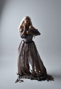 Full Length Portrait Of Girl Wearing Old Torn Wedding Dress. Standing Pose With Rim Lighting On A Grey Studio Background.