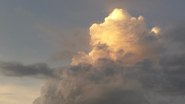 With a sunset illuminated towering cumulus stage cloud growing and forming taller, darker clouds pass in front of the rising cumulus as the sunset color fades from the cloud.