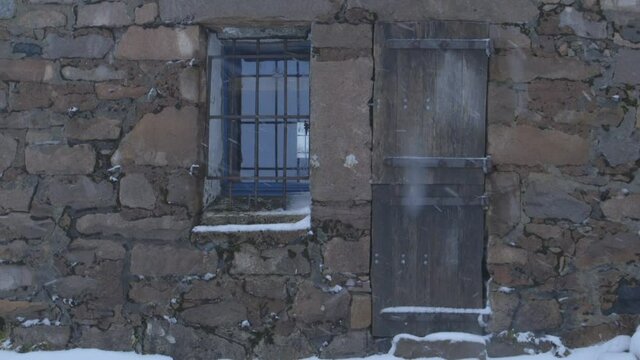 Tight static shot of Ben Nevis CIC hut with snow blowing through frame.