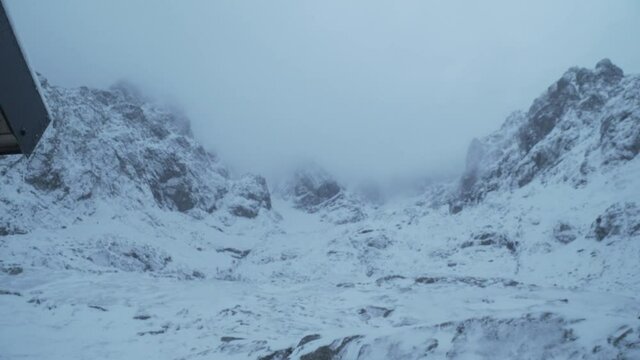 Shot pans to the right from the front door of Ben Nevis CIC hut revealing cloud and snow covered mountains in the distance. Scotland.
