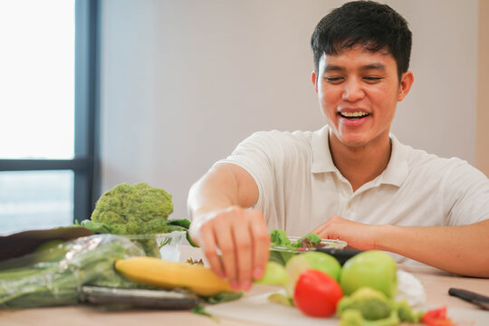 Close Up Young Asian Man Eating Vegetable Salad With Fruit On Table In Kitchen Room For Vegan Healthy Lifestyle Concept