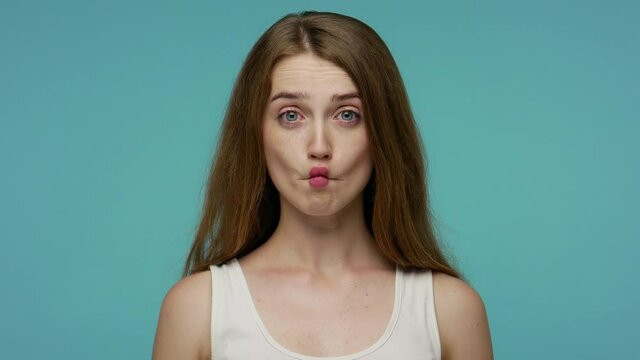 Surprised funny comical girl making fish face with pout lips and looking with shocked dumb idiotic expression, doing duck grimace, fooling around. indoor studio shot isolated on blue background