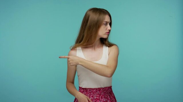 Annoyed offended girl in summer dress pointing get out, showing exit, asking to leave her alone, breaking up with friend, looking resentful vexed. indoor studio shot isolated on blue background
