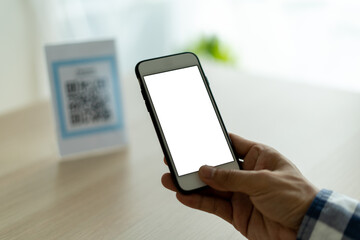 The man's hand is using a mobile phone to scan QR code. The man is scanning to use as a discount for food and drink in the Restaurant or Cafe. Pay without holding cash.
