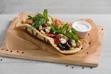Gyros with vegetables is  on a light wooden background.  Ingredients: grilled vegetables (eggplant, zucchini, bell pepper), cabbage with feta cheese and herbs, seasoned with Greek sauce, in a fragrant