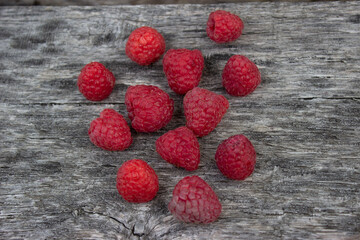 Ripe raspberries lie on a gray wooden surface. Scattered berries. Freshly harvested crop. Postcard,...