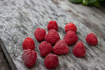 Ripe raspberries lie on a gray wooden surface. Scattered berries. Freshly harvested crop. Postcard,...