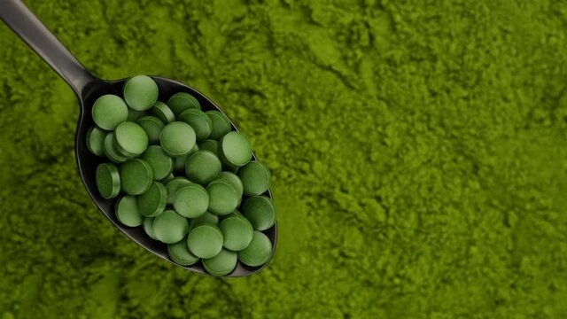 chlorella tablets in spoon and chlorella powder on background