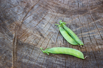 Young green peas in pods. Three pieces lie on a wooden surface. Postcard, banner.