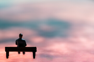 Miniature figurine posed as man sitting alone on a bench in surreal scenery, minimalist abstract concept image - 360401745