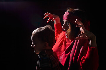 Woman in red sweater and the turban of wizard or sorcerer with boy on black background. Actress...