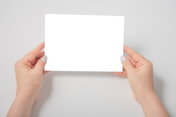 Women's hands holding a blank paper sheet, on gray. Mockup of a blank sheet of paper