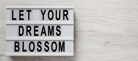 'Let your dreams blossom' on a lightbox on a white wooden background, top view. Space for text.