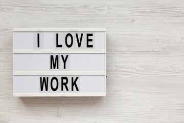 'I love my work' on a lightbox on a white wooden background, top view. Flat lay, from above, overhead. Copy space.