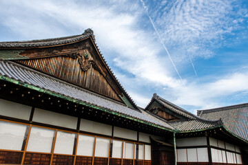 Fototapeta na wymiar Nijo Castle ancient carved wooden roofs with blue sky and aircraft contrails in the background, Kyoto, Japan. 