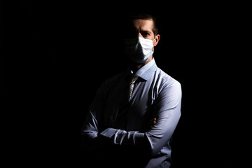 A businessman in a medical mask, a slave and a tie crossed his arms on his chest. black background, isolated