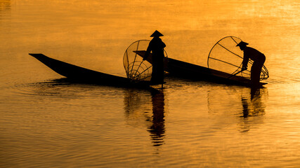 A fisherman show catches fish for food in sunrise rays at Inle lake ,Myanmar .Intha people lifestyle with blue white cloud sun sky