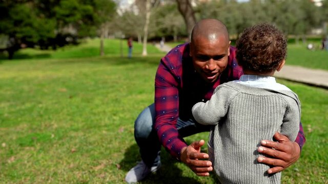 Adorable African American little boy playing with dad. Happy father hugging son on green lawn in city park at summer. Family and weekend concept