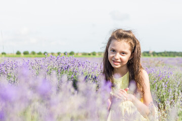 Fototapeta na wymiar A little girl wearing yellow dress, posing in a lavender field before sunset. Selective focus.
