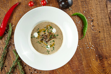 Diet mushroom cream soup in a white plate on a wooden background in a composition with ingredients