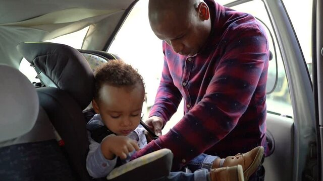 African American bald dad checking belts on child car seat. Focused young father protecting in case of emergency. Safety and transportation concept