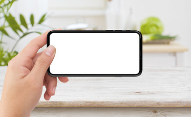 Left hand holding white mobile smartphone device in kitchen