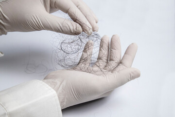 Hair loss specialist wearing gloves, picking up your hair for examination. On white background in clinic with copy space.