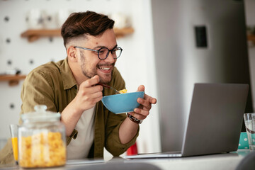 Young man eating breakfast and reading the news online. Handsome man enjoying at home.	
