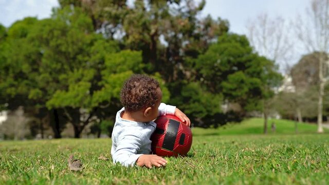 Mixed-race little boy playing with ball and falling down on lawn. African American father rising his son and boy kicking ball. Childhood, summer and weekend concept