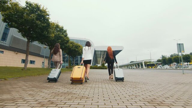 three happy girls go on vacation and go to the airport with luggage in their hands. Tourist Rest or travel of women without men.