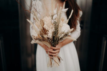 a bride posing outdoors with her bouquet of dried flowers in her hand