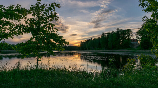 image with a beautiful colorful sunset over the lake, in the foreground the contours of trees and grass, Lielais Ansis, Rubene, Latvia