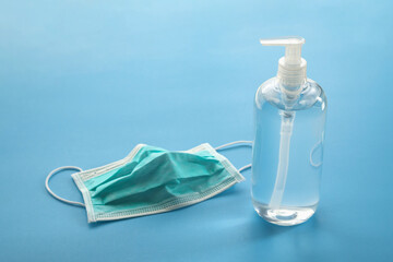 Alcohol hand sanitizer gel bottle with surgical face mask on blue background protection against COVID-19 coronavirus. Healthcare and medical concept