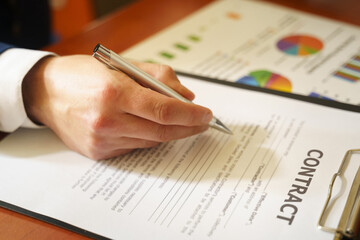 Businessman sitting at office desk signing a contract with shallow focus on signature.