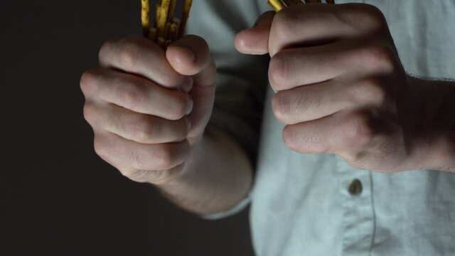 Caucasian man baker breaks salty bread sticks into two parts. Close-up of a breaking bread.
