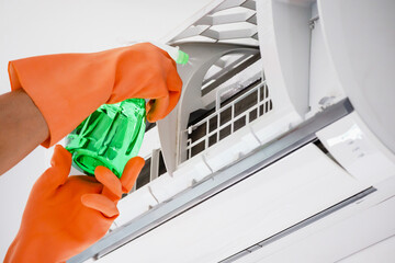 Asian man cleaning air conditioner with spray bottle