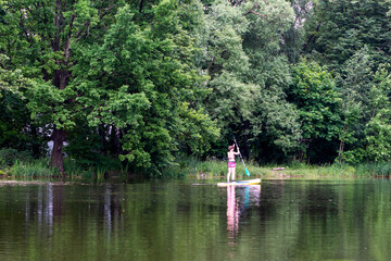 Fototapeta na wymiar Landscape pond in the park. Woman on a board with a paddle