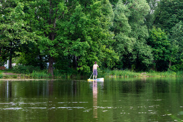 Fototapeta na wymiar Landscape pond in the park. Man on a board with a paddle