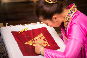 Traditional Isan Thai silk weaving. Asian woman embroidering golden thread on silk. Yong woman are...