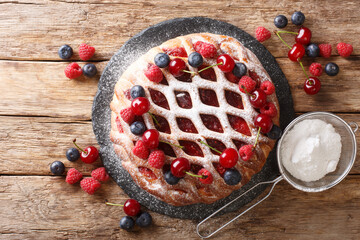 crostata pie with raspberries, blueberries and cherries sprinkled with powdered sugar close-up on a slate board. horizontal top view
