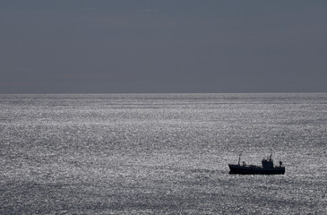Silhouet of a fishing boat which floats on waving water with ripples in Iceland