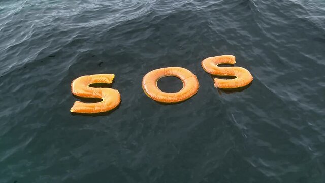Sos word on water waves. Sos inflatable orange symbol sailing on dark water. Save our souls concept idea. Emergency call minimal concept. Help mesage on water ocean waves.