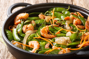 Fried shrimp recipe with onions, carrots and pods of snow peas close-up in a pan. horizontal