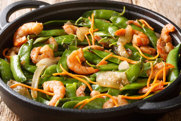 Healthy food of fried shrimp with onions, carrots and pods of snow peas close-up in a plate on the table. horizontal