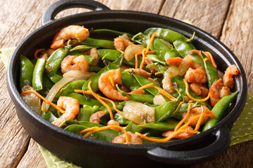 Asian stir-fried shrimp with onions, carrots and pea pods close-up in a plate. horizontal