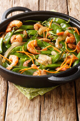 Tasty fried shrimp with onions, carrots and pea pods close-up in a plate on the table. vertical