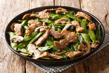 Stir-fried meat with mushrooms and pea pods, garlic, sesame seeds in soy sauce close-up in a plate on the table. horizontal